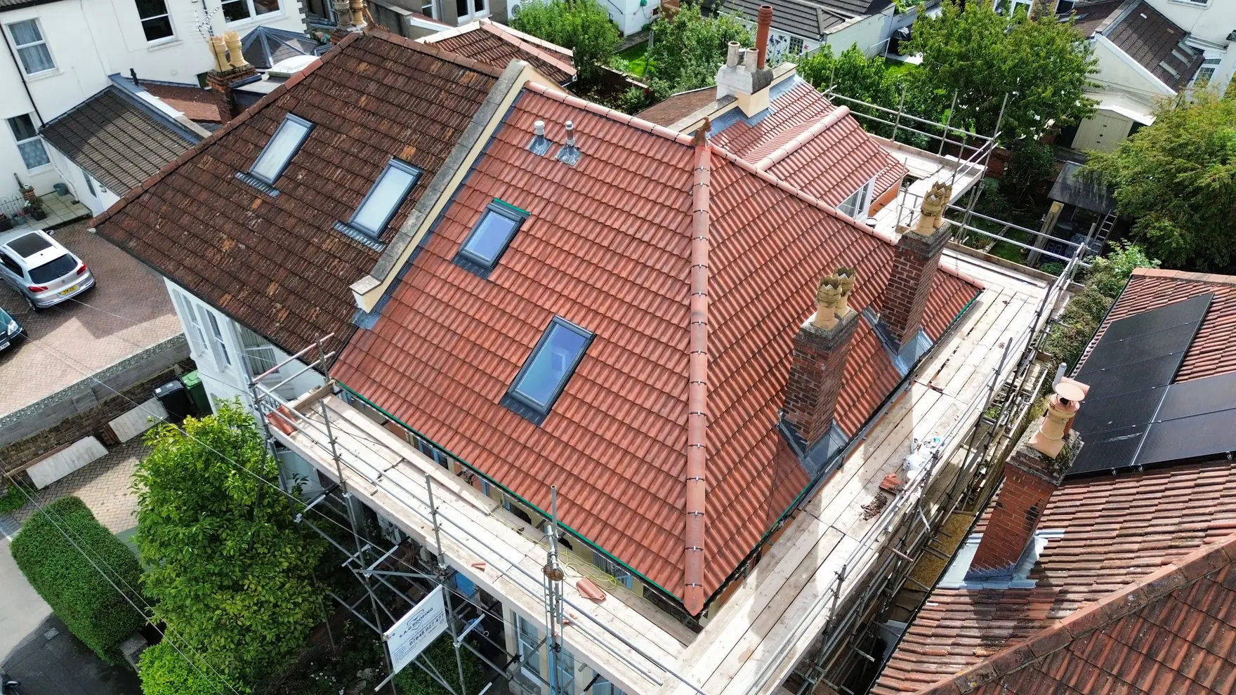 Aerial view of a completed re-roof in Bristol, new red interlocking tiles with rooflights and scaffold still in place